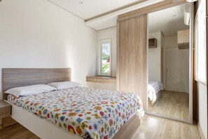 A bedroom with a bed, a nightstand, a window, and a door leading to another room. - Casa Canasvieiras (Florian ópolis)