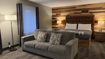 Une chambre d’hôtel avec un canapé, un lit doté d’une tête de lit en bois, une table de chevet et une lampe sur pied.