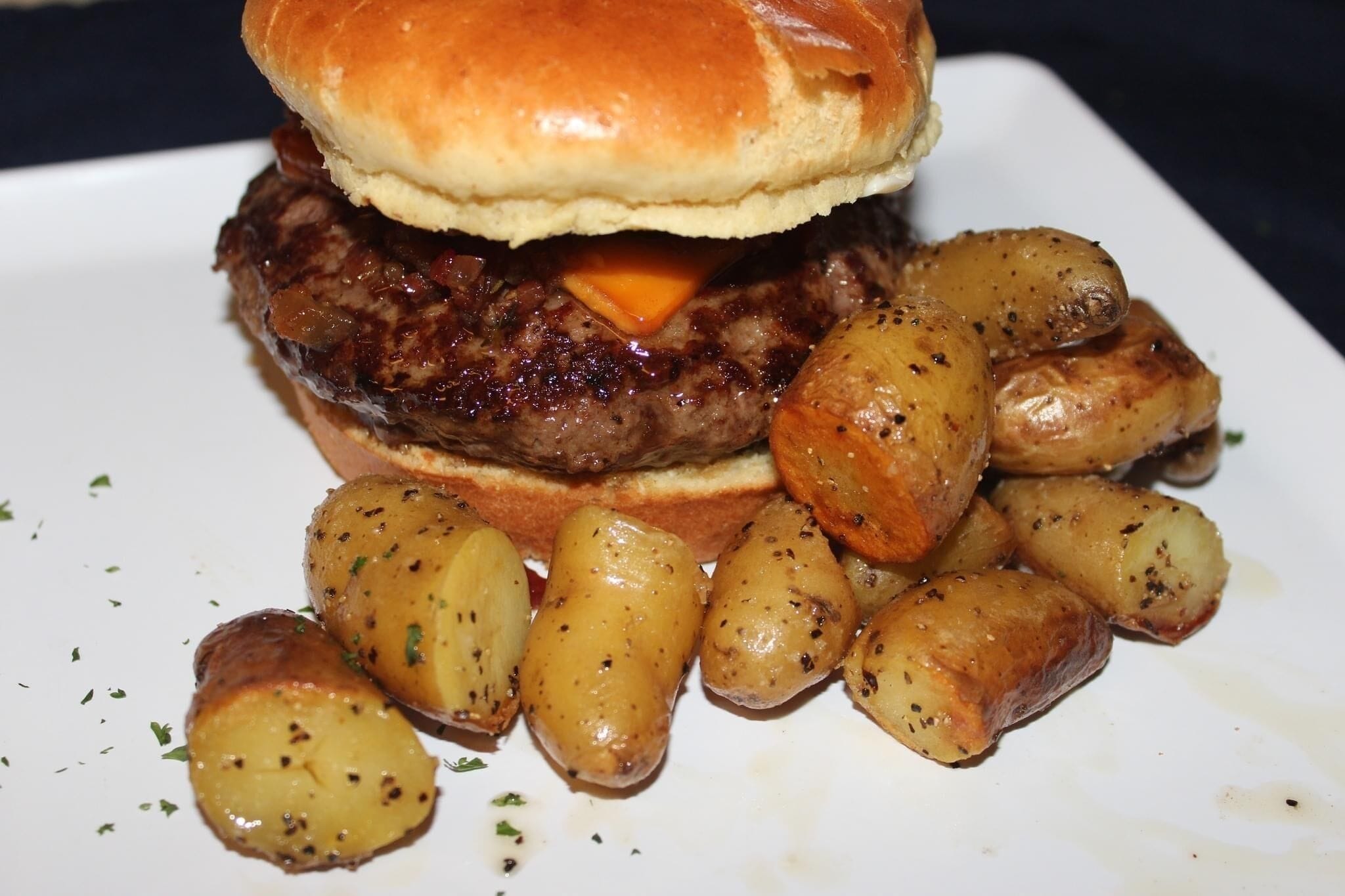 Una hamburguesa con carne, queso y pan, acompañada de patatas asadas.