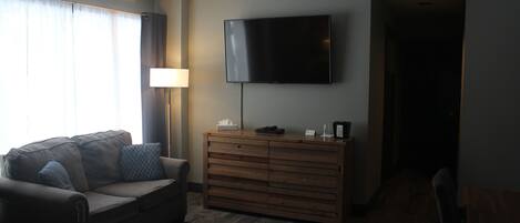 Une chambre d’hôtel avec un canapé, une commode en bois, un téléviseur à écran plat fixé au mur et une lampe.