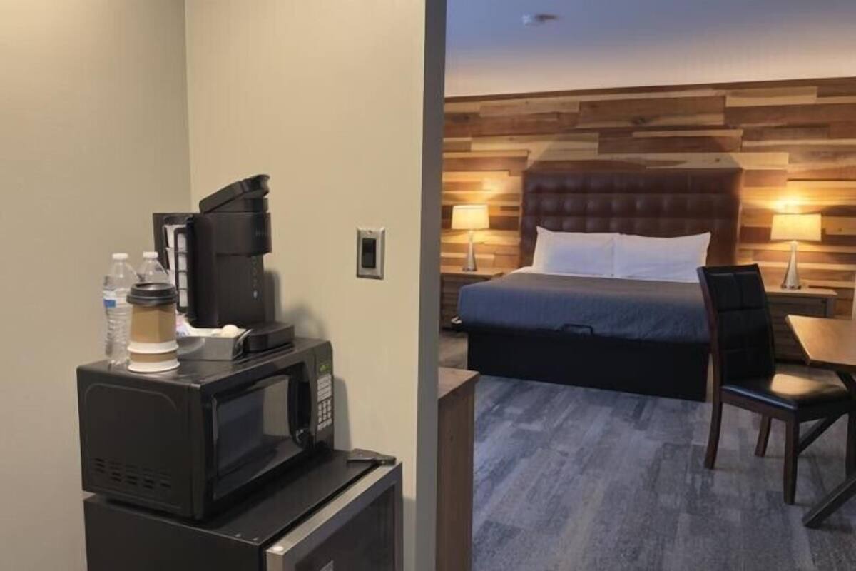 Een hotelkamer met een bed, een bureau, een magnetron, een koffiezetapparaat en een waterfles.