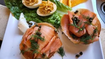 A plate with two open-faced sandwiches topped with smoked salmon and capers, a boiled egg, and a side of orange slices.