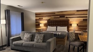 Een hotelkamer met een grijze bank, een bed met een houten hoofdeinde, een klein tafeltje en een lamp.