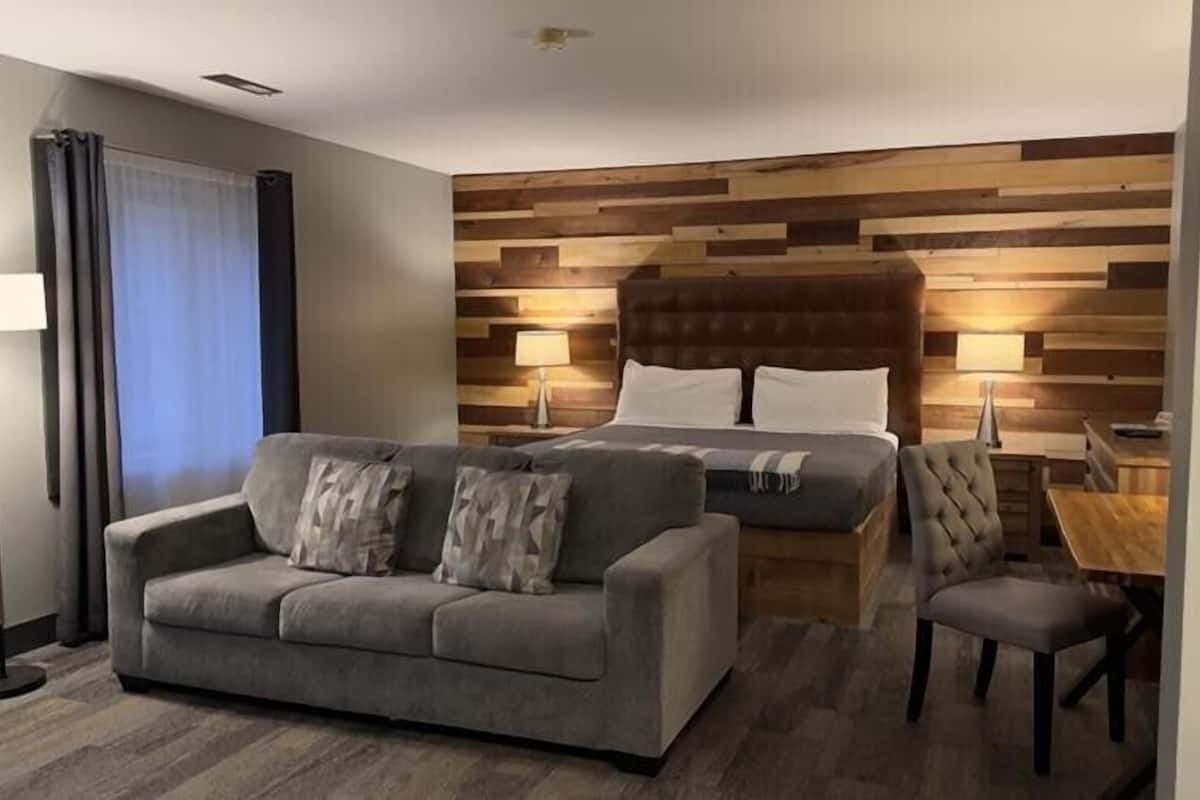 Een hotelkamer met een grijze bank, een bed met een houten hoofdeinde, een klein tafeltje en een lamp.