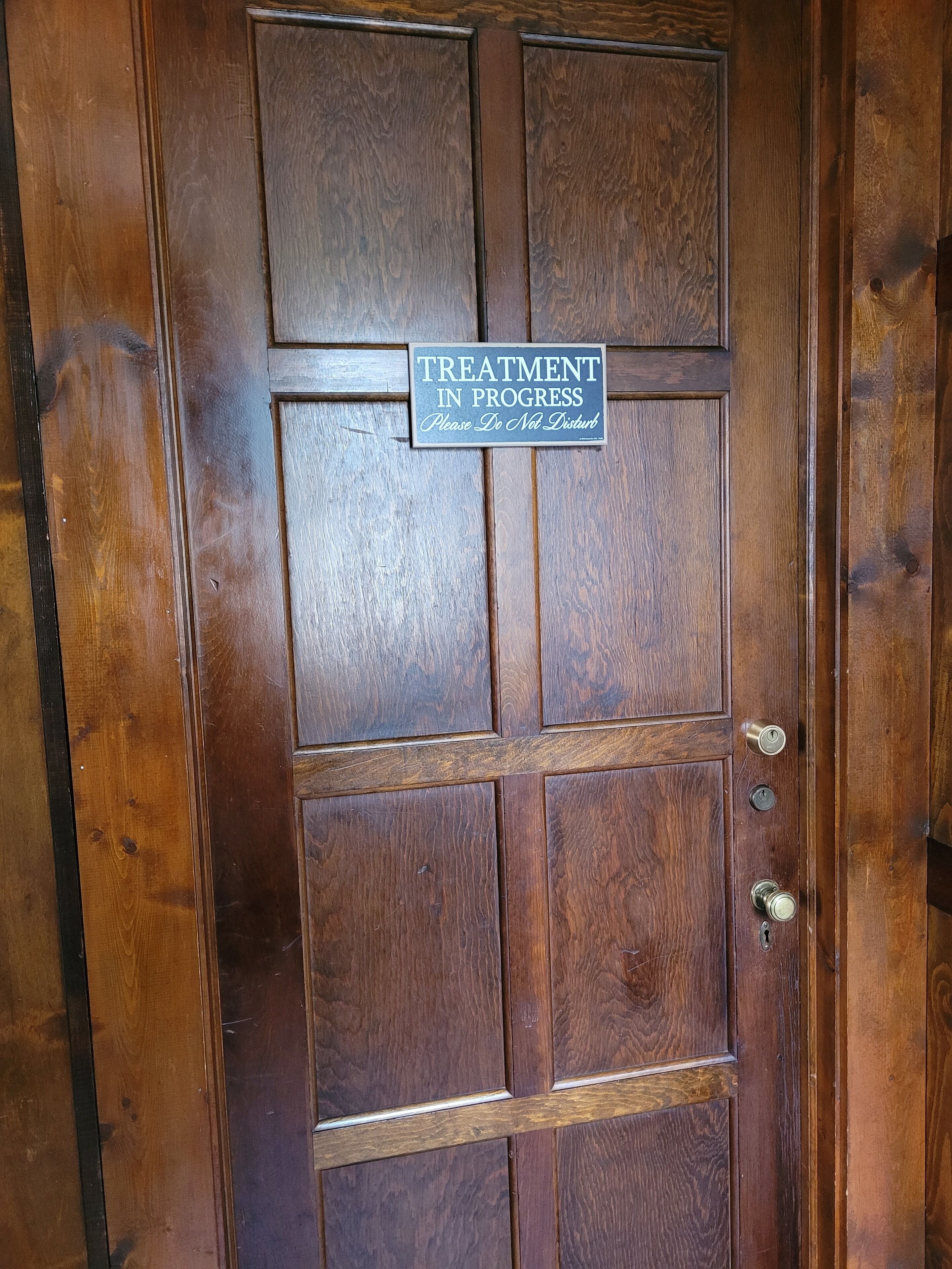 A wooden door with a sign that reads "TREATMENT IN PROGRESS Please Do Not Disturb."