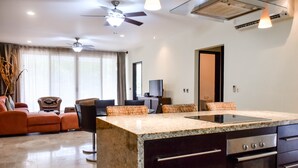 A modern living room with a large island, dark wood cabinets, a ceiling fan, and a television in the background. - Mamitas Village by Casago (Playa del Carmen)