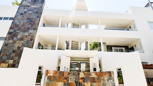 A modern multi-story building with a prominent stone facade and balconies. - Mamitas Village by Casago (Playa del Carmen)