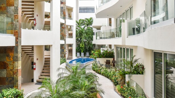 A multi-level atrium with a central pool, surrounded by lush greenery and modern architecture. - Mamitas Village by Casago (Playa del Carmen)
