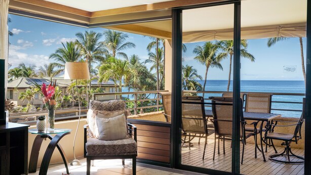 Uma varanda com vista para o oceano, mobiliada com cadeiras e uma mesa, e um vaso com planta.