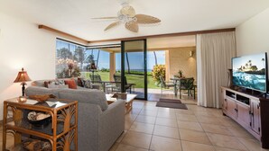Sala de estar com sofá, mesa de centro, televisão e vista para o oceano através de amplas portas de vidro.