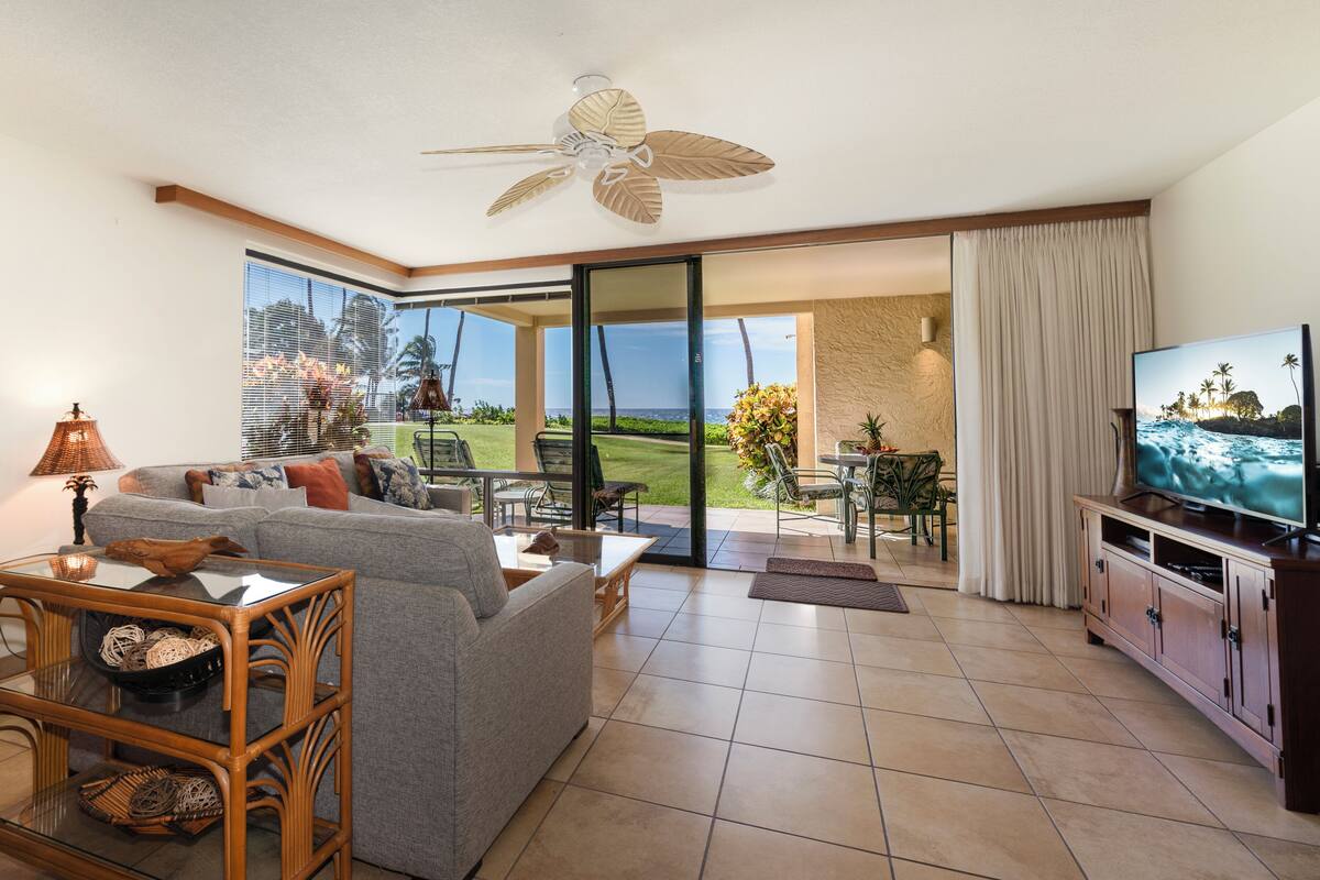 A living room with a sofa, coffee table, TV, and a view of the ocean through large glass doors.