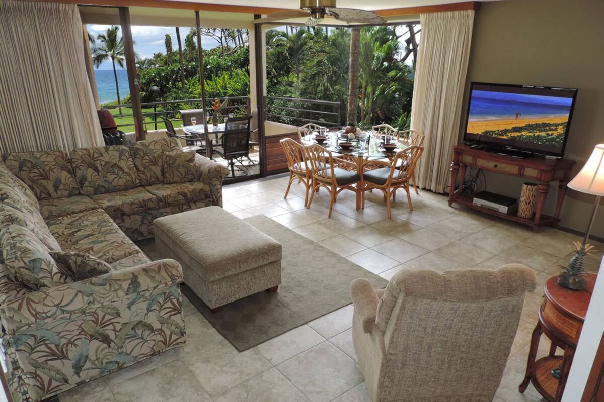 A living room with a sofa, ottoman, dining table, chairs, and a TV.