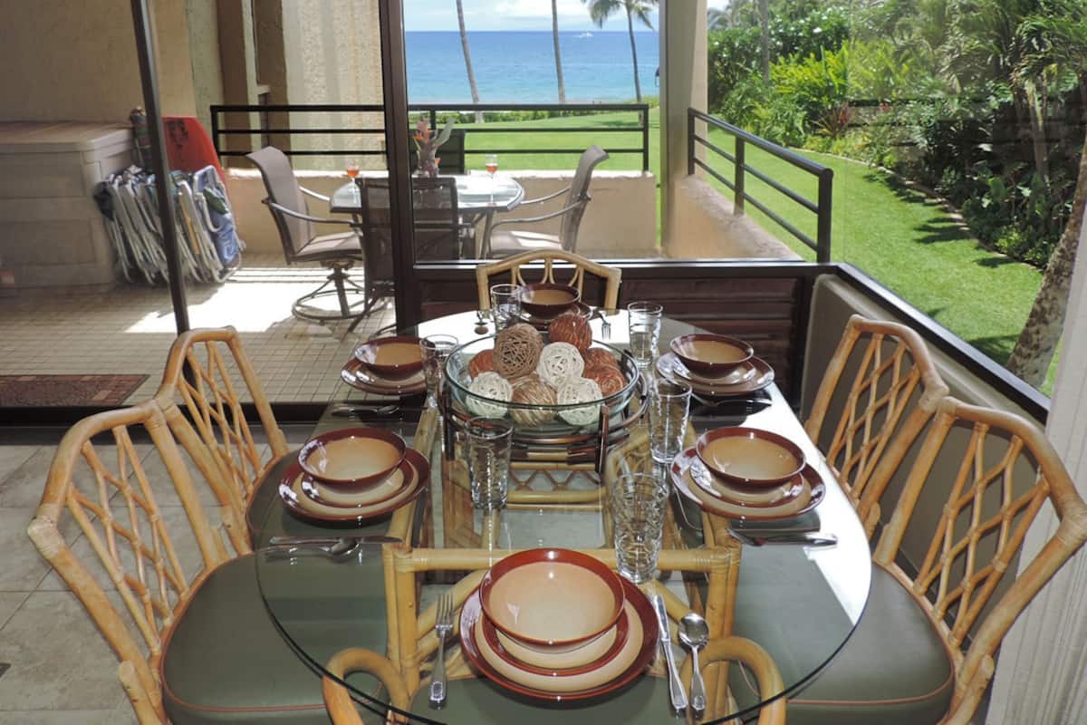 A dining table set with plates, glasses, and cutlery on a balcony overlooking the ocean.