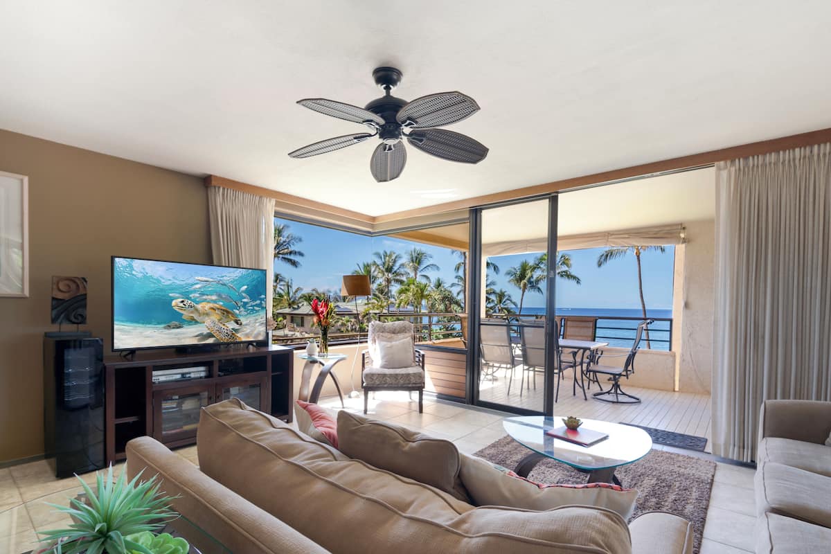 A living room with a television, sofa, and a balcony with a view of the ocean.