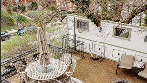 Una terraza con una mesa redonda y sillas, un hogar para fuego y una estructura tipo casa rodante blanca con ventanas y faroles.