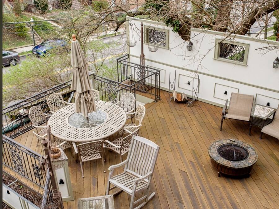 Una terraza con una mesa redonda y sillas, un hogar para fuego y una estructura tipo casa rodante blanca con ventanas y faroles.