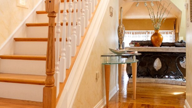 Una escalera con escalones de madera y balaustres blancos, que conduce a una plataforma con una mesa de centro de vidrio y objetos decorativos.