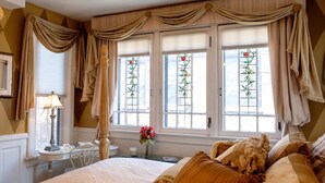 Un dormitorio con una cama grande, un escritorio con lámpara y una ventana con cortinas.
