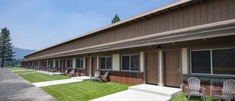 A row of single-story buildings with numbered doors, outdoor seating, and a well-maintained lawn.