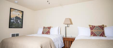 A hotel room with two beds, a ceiling fan, a lamp, and a poster on the wall.