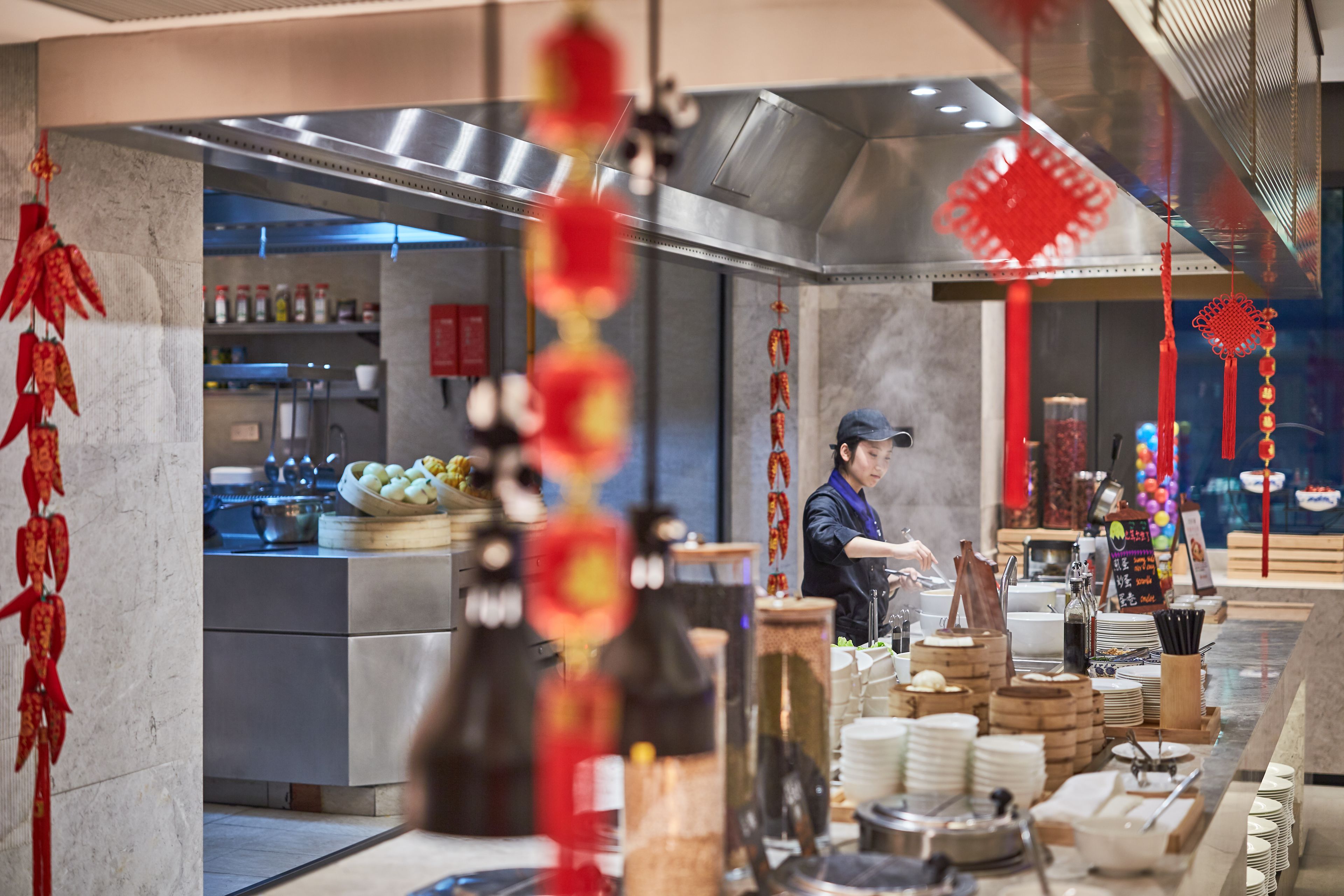 Interior de un restaurante con zona de cocina, mesas de buffet y decoración roja.