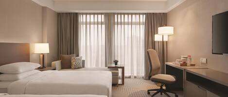 A hotel room with two beds, a desk, a chair, a TV, and a window with curtains.