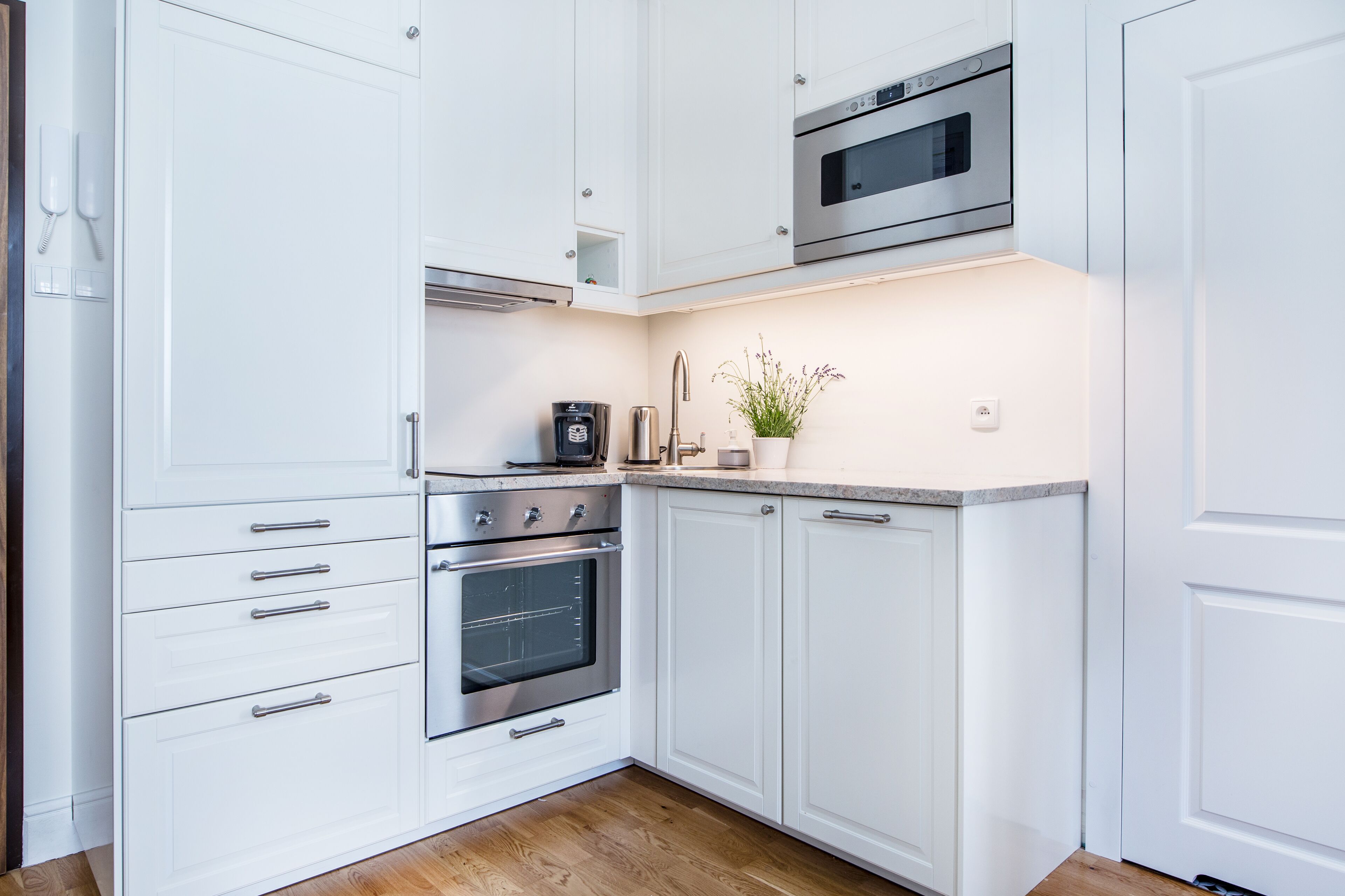 A modern kitchen with white cabinetry, stainless steel appliances, and a built-in oven.