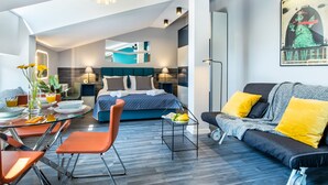 Una habitación de hotel moderna con cama, sofá, zona de comedor y una pequeña mesa con sillas.