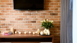Una sala de estar con una pared de ladrillo, un televisor de pantalla plana montado sobre una consola de madera, y una mesa redonda con manzanas verdes.