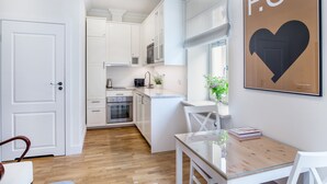 Una cocina moderna con armarios blancos, un comedor con mesa de vidrio y un cartel enmarcado en la pared.