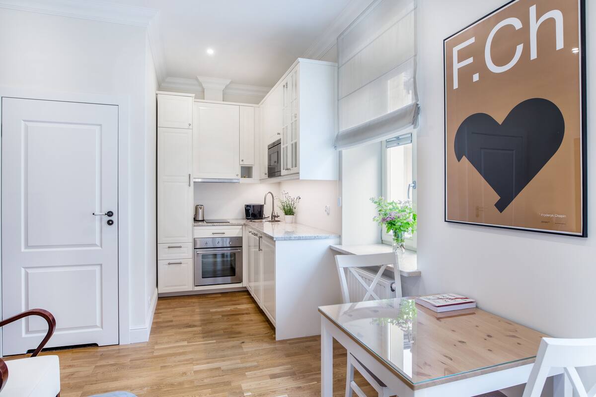 A modern kitchen with white cabinetry, a dining area with a glass table, and a framed poster on the wall.