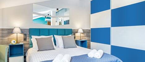 A modern hotel room with a large bed, two bedside tables, a mirror, and a view of the hotel's interior.