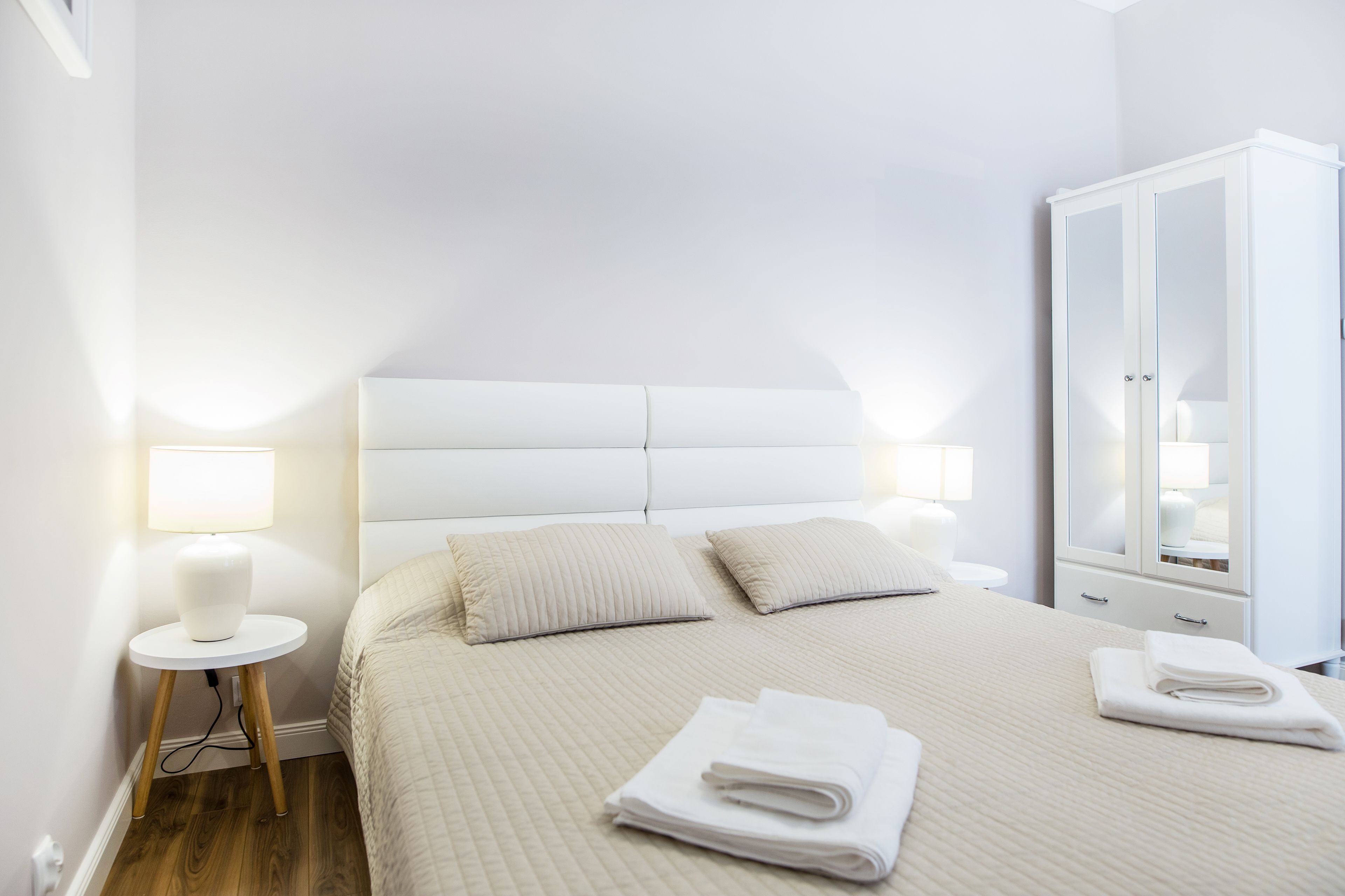 Un lit bien fait, avec une tête de lit, deux oreillers, une lampe de chevet et une serviette pliée posée sur le sol.