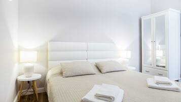 Un lit bien fait, avec une tête de lit, deux oreillers, une lampe de chevet et une serviette pliée posée sur le sol.