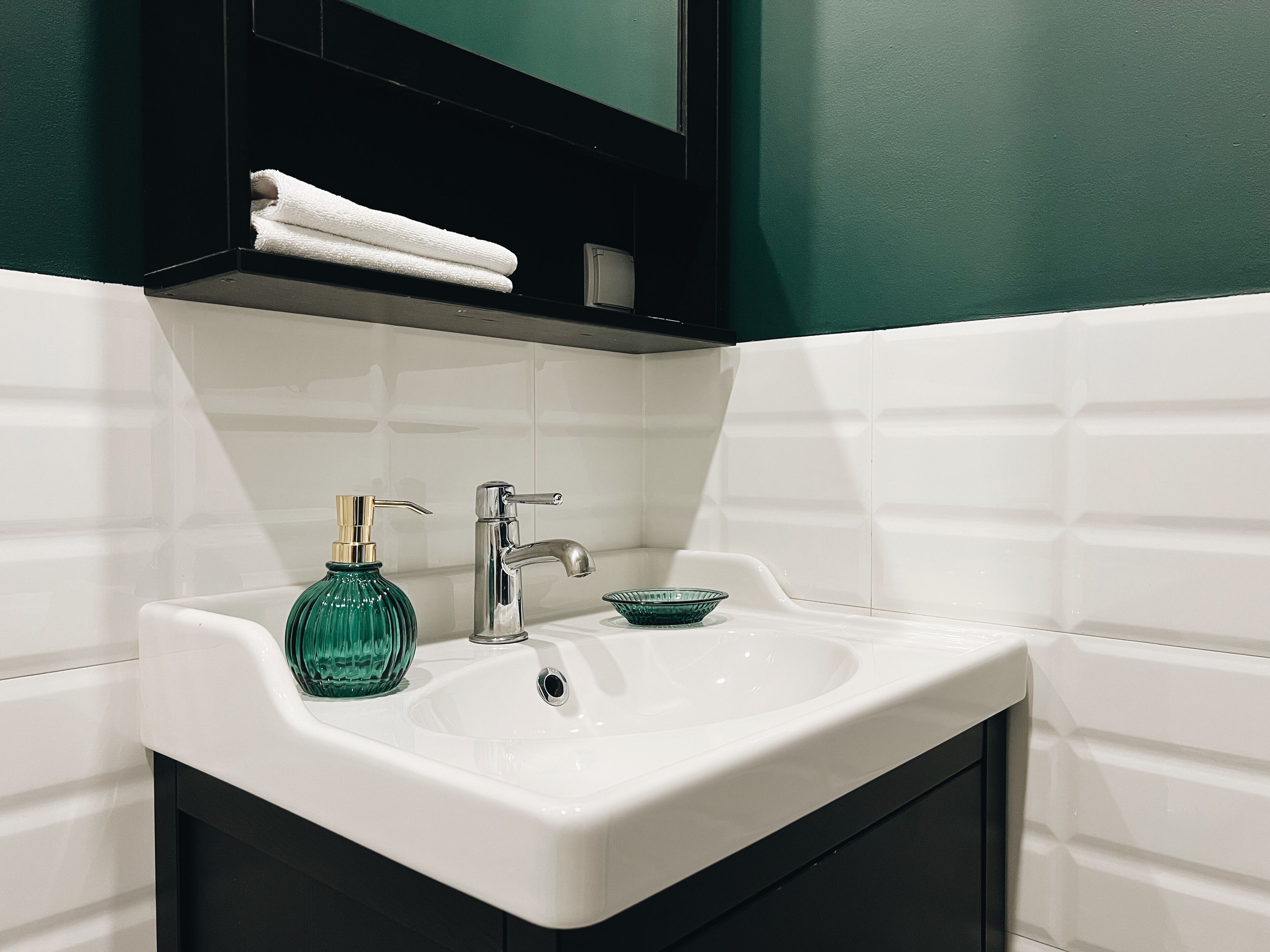 A bathroom with a white sink, a green glass soap dispenser, and a small blue bowl.