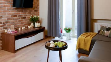 Una sala de estar moderna con una pared de ladrillo, un televisor de pantalla plana, un mueble de madera para entretenimiento, un sofá, una mesa de centro con frutas y vistas a través de una ventana con cortinas.