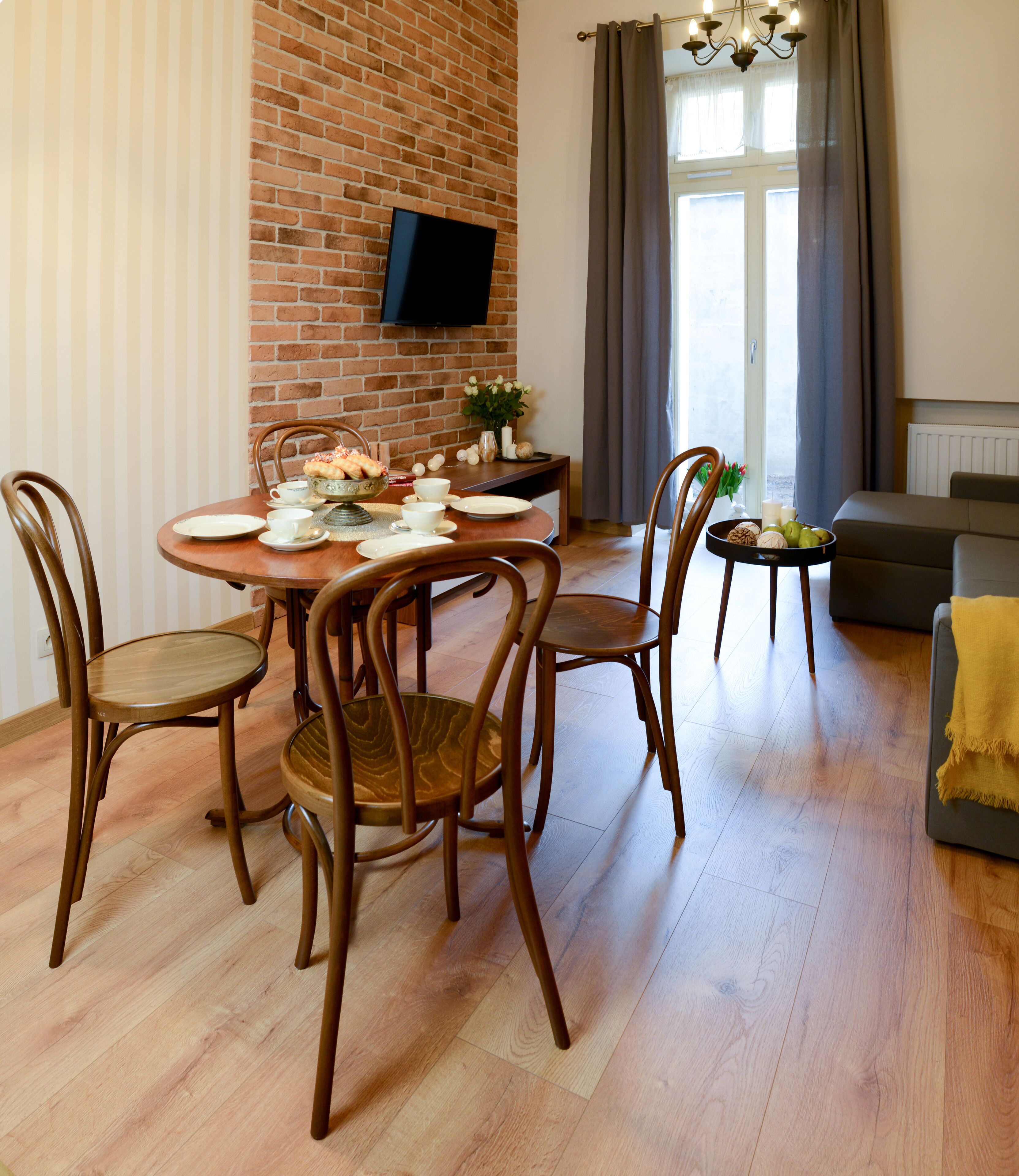 Un comedor con pared de ladrillo, un televisor de pantalla plana sobre una mesa preparada para cuatro comensales y un sofá al fondo.