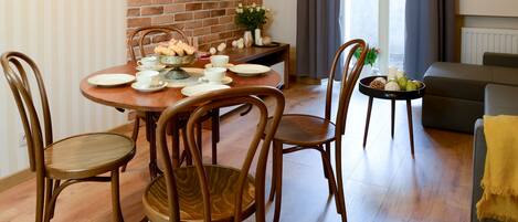 Un comedor con pared de ladrillo, un televisor de pantalla plana sobre una mesa preparada para cuatro comensales y un sofá al fondo.