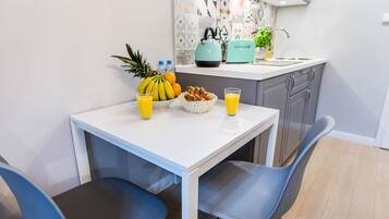 A modern kitchen with a white table, blue chairs, a fruit basket, and a toaster.