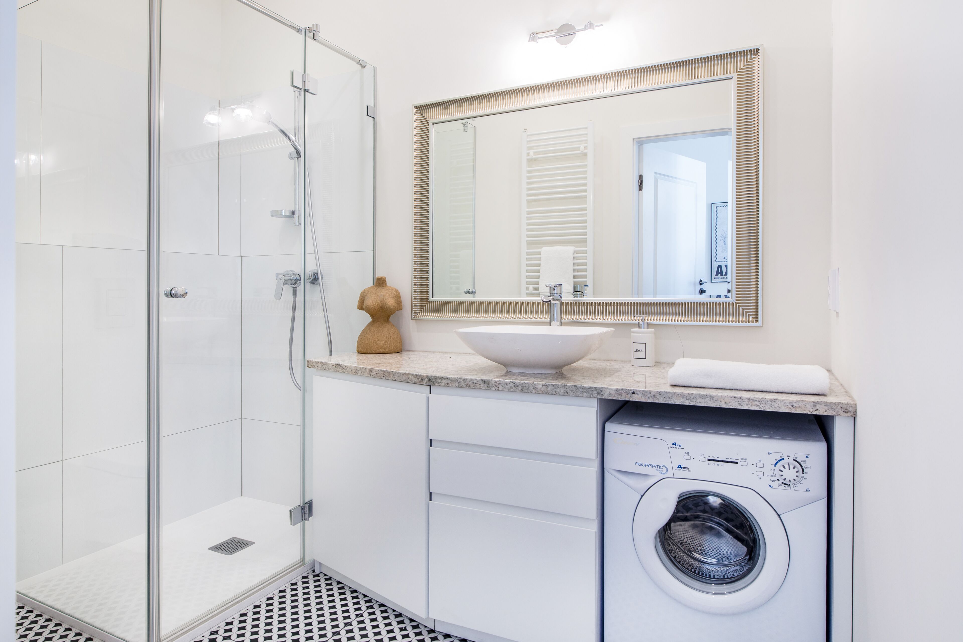 A modern bathroom with a glass shower enclosure, a sink with a vessel basin, a large mirror, and a front-loading washing machine.