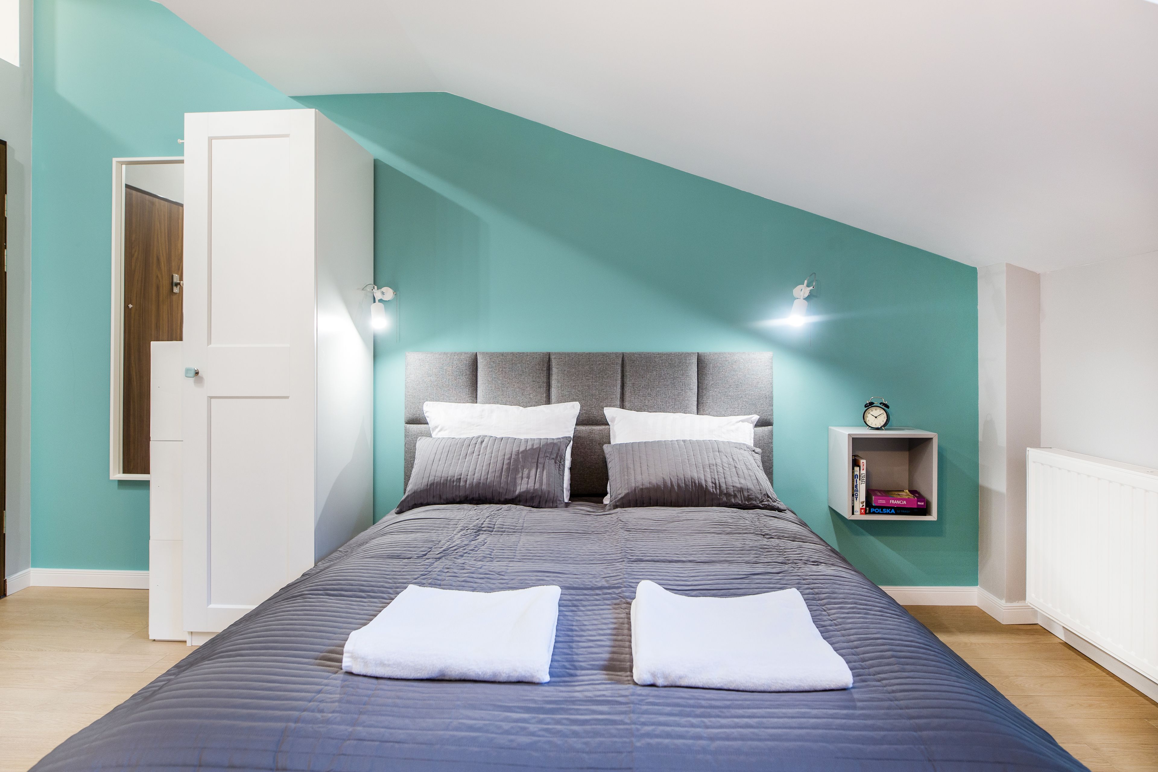 A bedroom with a bed, pillows, a nightstand, and a wall-mounted shelf.