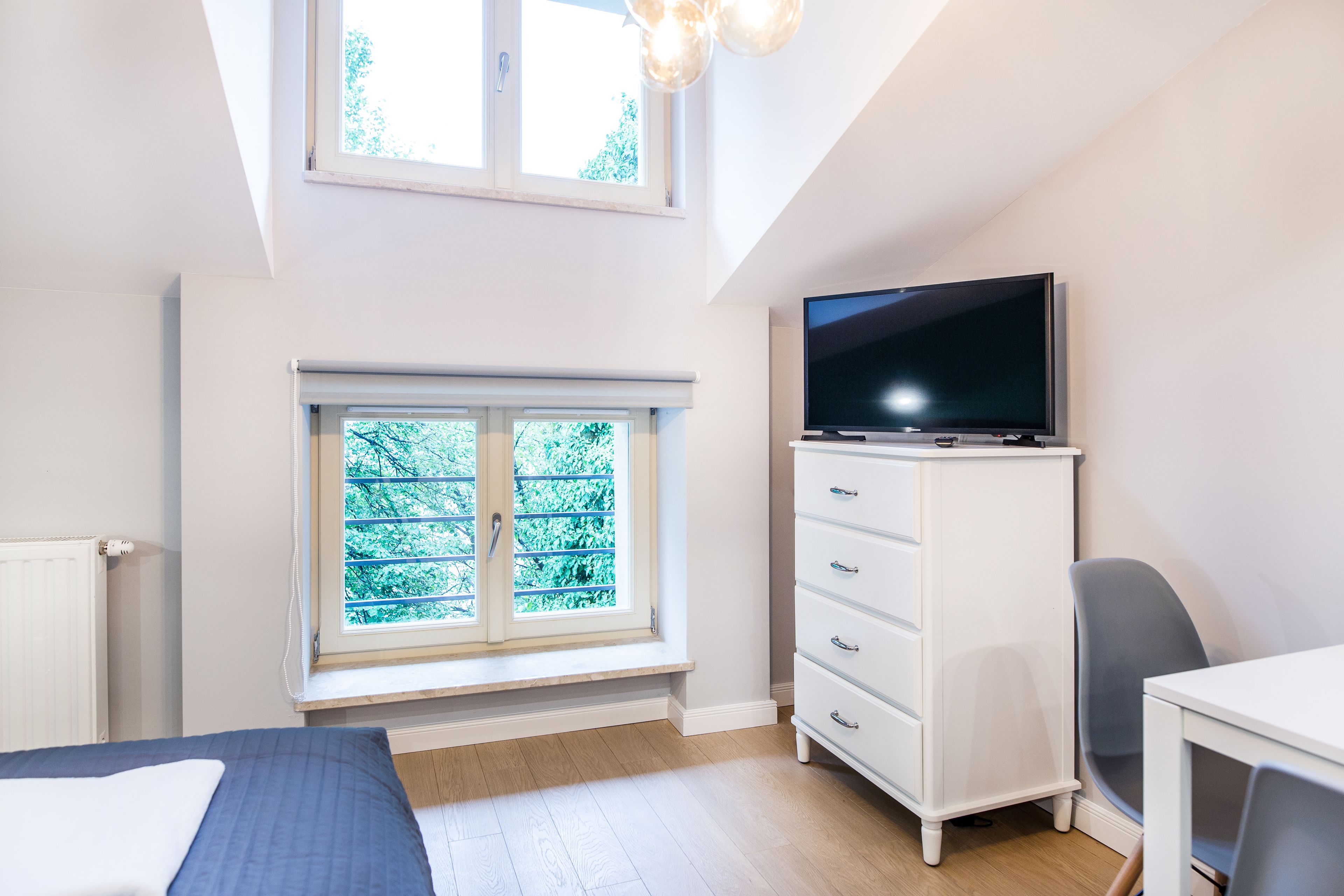 Une chambre à coucher avec un lit, une télévision, une commode et une fenêtre donnant sur des arbres.