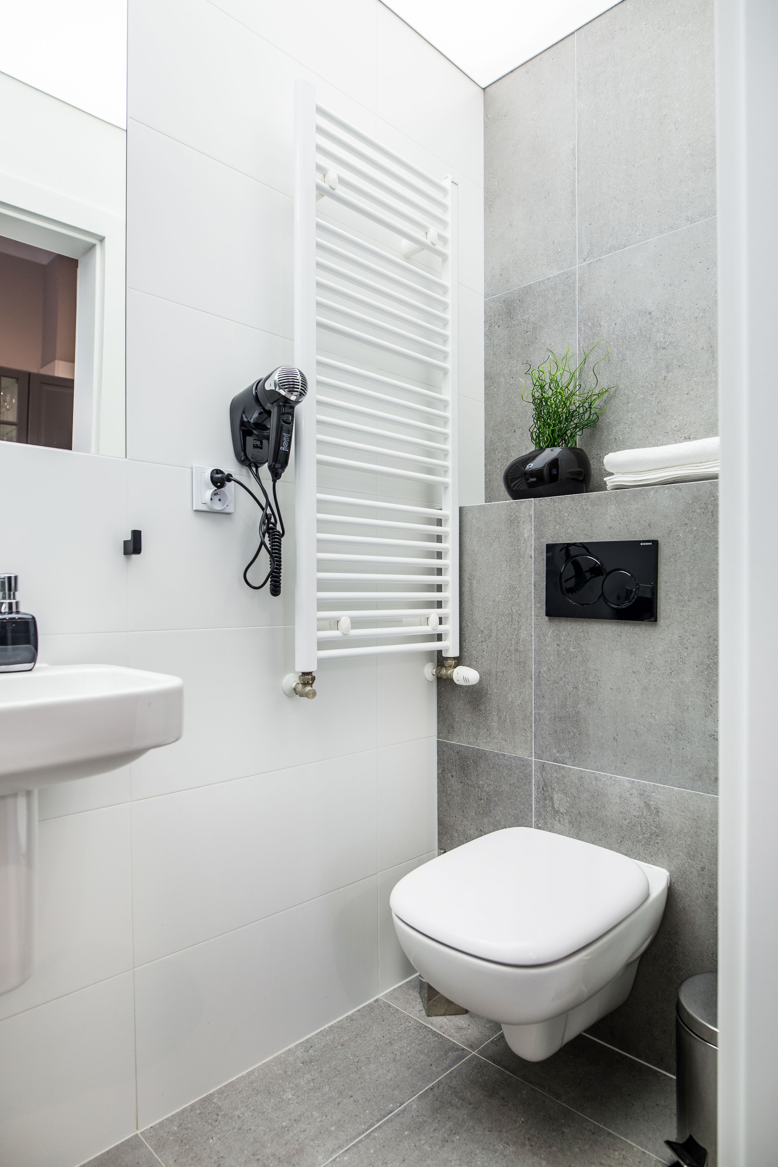 A modern bathroom with a white sink, a toilet, a towel rack, a hairdryer, and a radiator.
