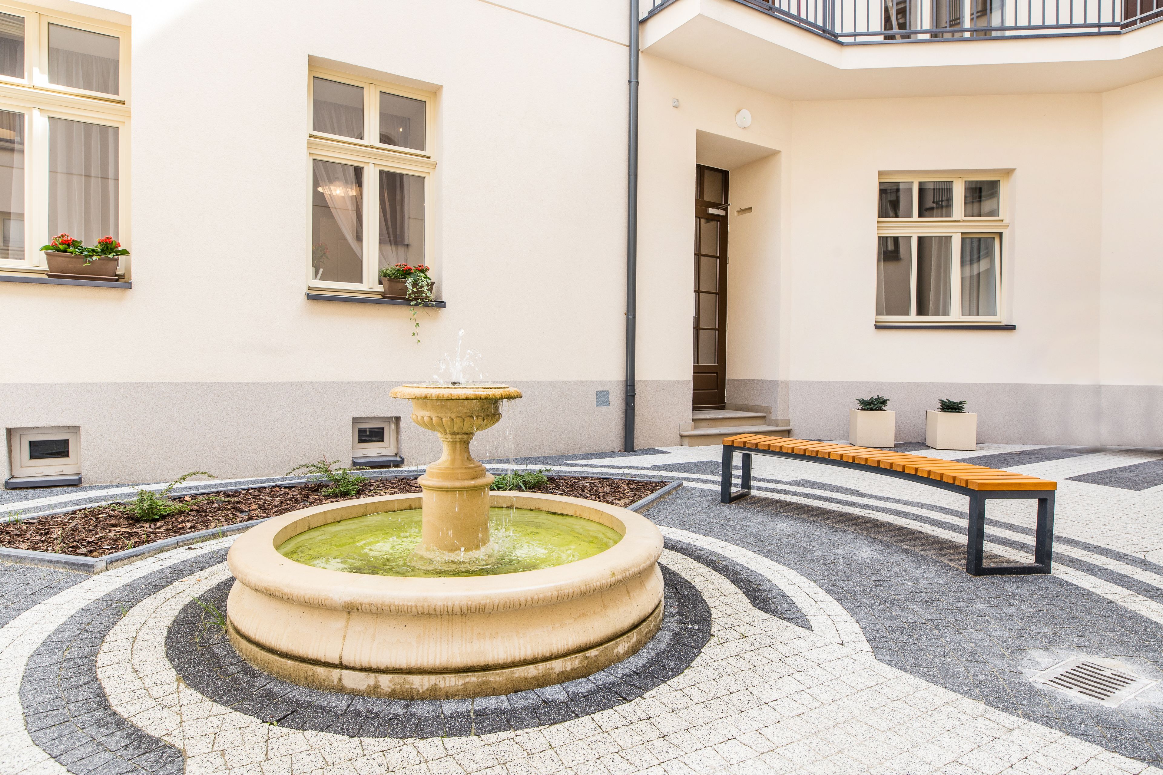A courtyard with a central fountain, a bench, and potted plants.