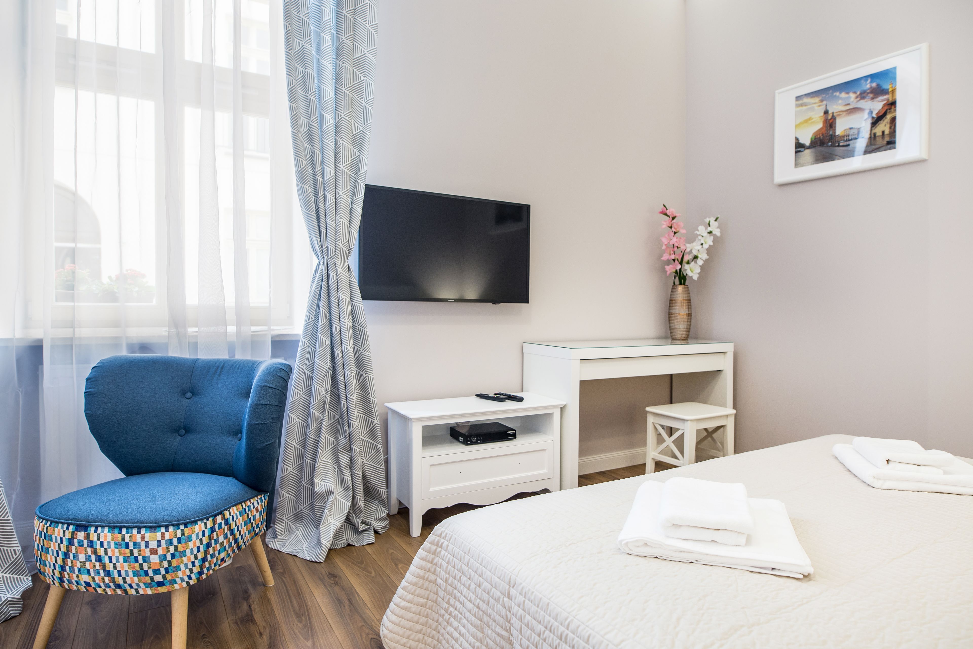 Una habitación de hotel con cama, escritorio con televisor, silla y ventana con cortinas.