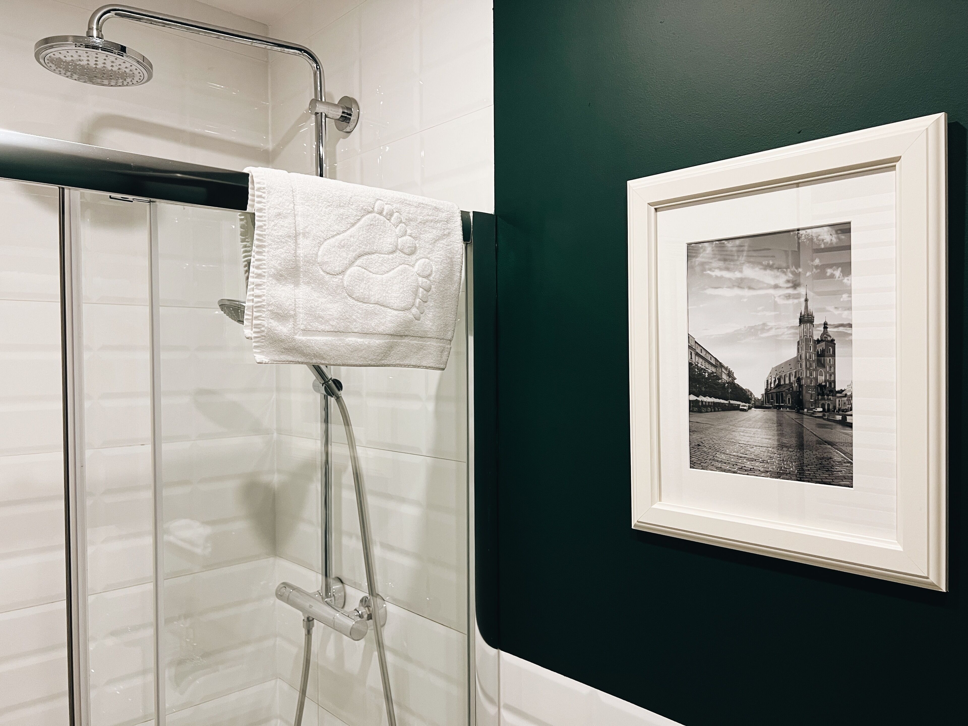 Un baño con cabina de ducha de vidrio, una toalla blanca y una fotografía en blanco y negro enmarcada en la pared.