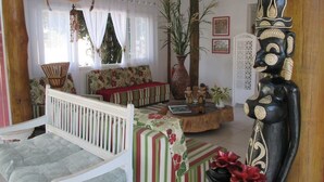 A cozy living room with a white sofa, a striped armchair, a wooden coffee table, and a decorative mask on the wall. - Pousada Cana Caiana (Paraty)