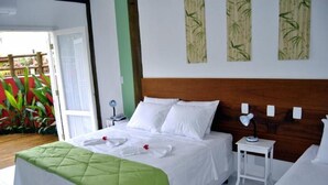 A hotel room with a large bed, a bedside table with a lamp, and a view of a garden. - Pousada Cana Caiana (Paraty)