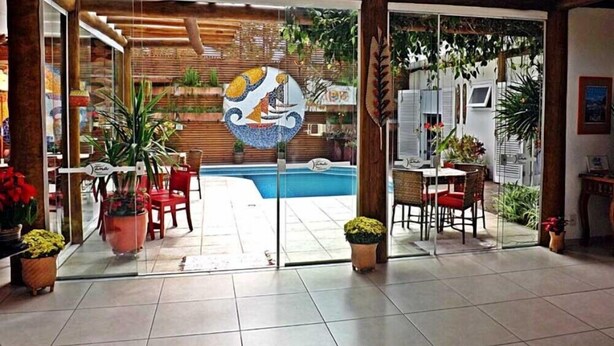 A hotel lobby with a glass door leading to a pool area, indoor plants, and a tiled floor. - Pousada Cana Caiana (Paraty)