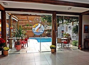 A hotel lobby with a glass door leading to a pool area, indoor plants, and a tiled floor. - Pousada Cana Caiana (Paraty)